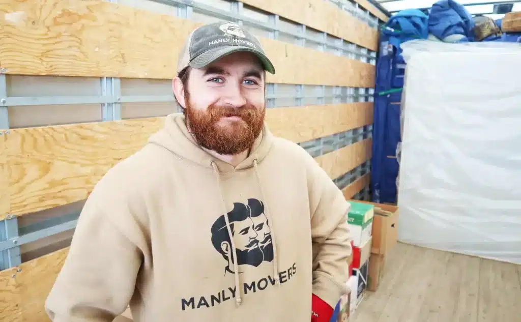 A bearded man in a hoodie, clarifying the cost of move, stands in a storage room.